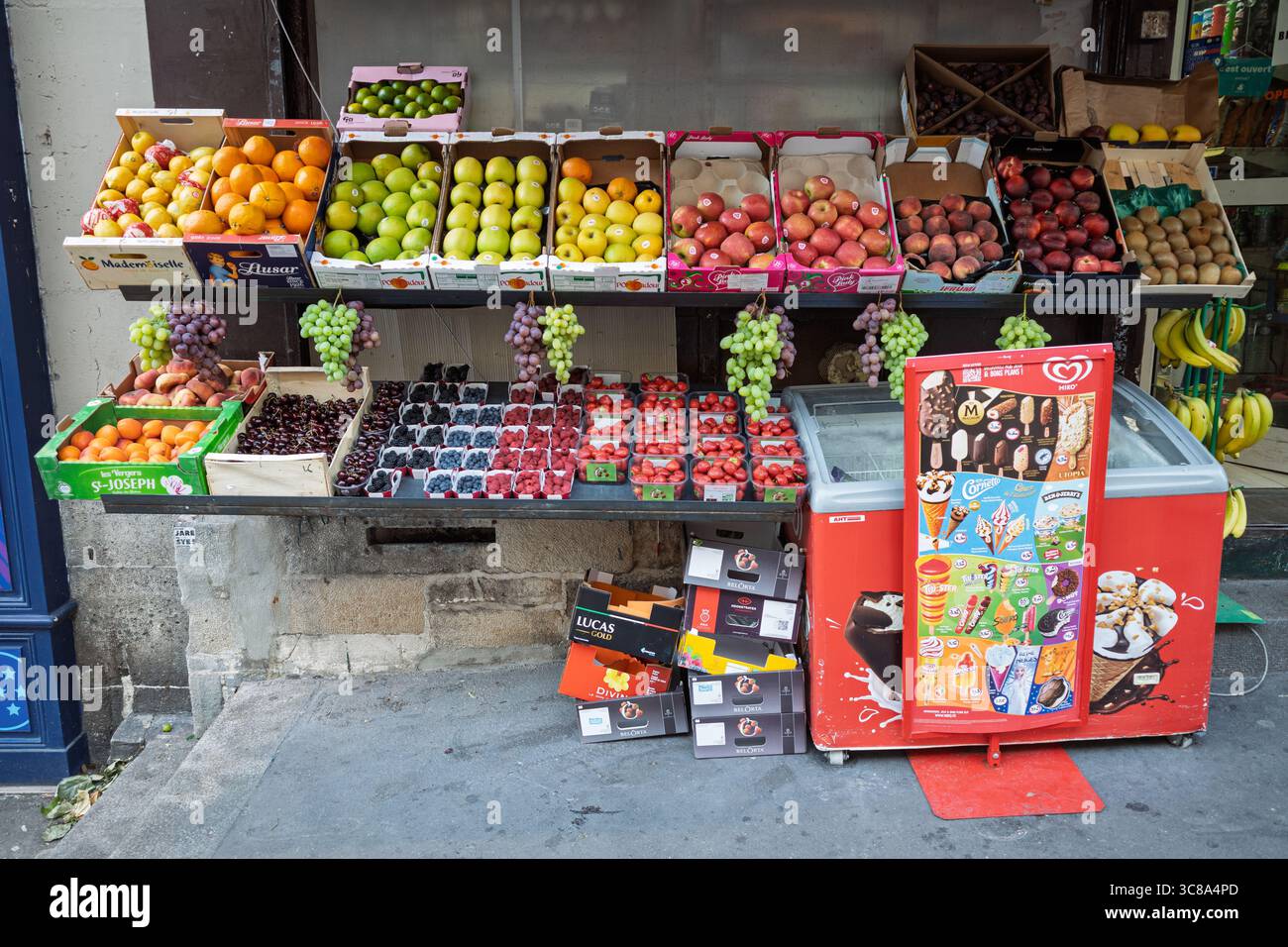 Un colorato stand all'aperto di frutta e verdura a Parigi, Francia, che espone prodotti freschi e un congelatore per gelati. Foto Stock