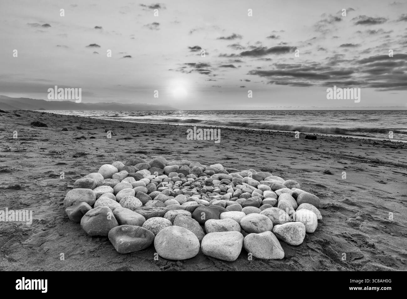 Le pietre rituali sacre per la cerimonia spirituale sono disposte in cerchio durante il tramonto sulla spiaggia bianco e nero Foto Stock