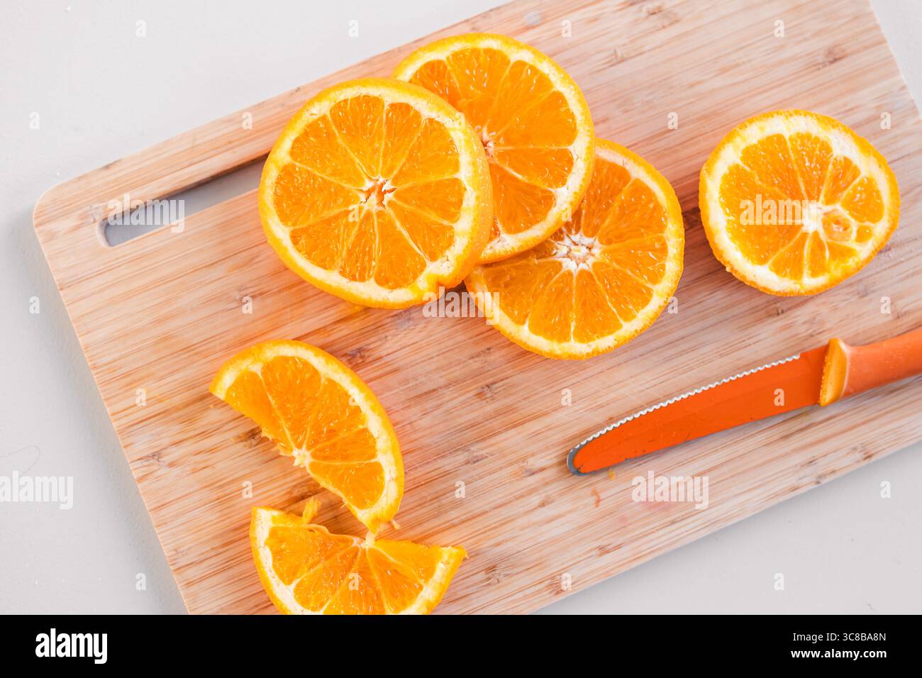 succose fette di arancia disposte su un tagliere di legno con un coltello arancione brillante, concetto di mangiare sano, frutta biologica e preparazione alimentare Foto Stock succose fette di arancia disposte su un tagliere di legno con un coltello arancione brillante, concetto di mangiare sano, frutta biologica e preparazione alimentare Foto Stock