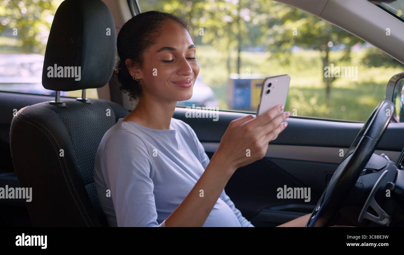 Donna afroamericana incinta ragazza auto auto auto auto veicolo gravidanza futura madre utilizzando telefono cellulare smartphone smartphone chattare autista Foto Stock