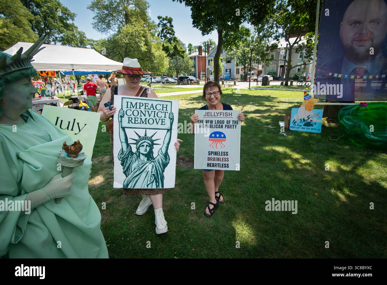 Cambridge, ma, Stati Uniti, 2 CD agosto 2025. Quasi 1.000 persone hanno partecipato alla “RABBIA CONTRO IL REGIME” in un mite sabato pomeriggio estivo sul Cambridge Common, di fronte all’Università di Harvard. L'evento della comunità organizzato da 50501, un movimento di base fondato per resistere alle politiche anti-democratiche dell'attuale governo federale degli Stati Uniti. Sono stati inclusi anche un certo numero di altri gruppi locali pro-democrazia e anti-Trump. Una donna dimostrante vestita da Statua della libertà ride con altre due donne di fronte a un enorme Meme del Vice Presidente J.D. Vance appoggiato contro un albero nel parco. Foto Stock