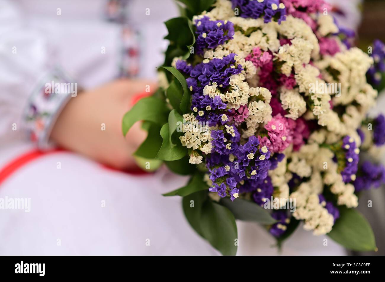 Giovane donna in abito tradizionale ricamato con bouquet di fiori selvatici. Primo piano di bouquet floreale in mano, adornato in costume popolare. Donna in Ucraina Foto Stock
