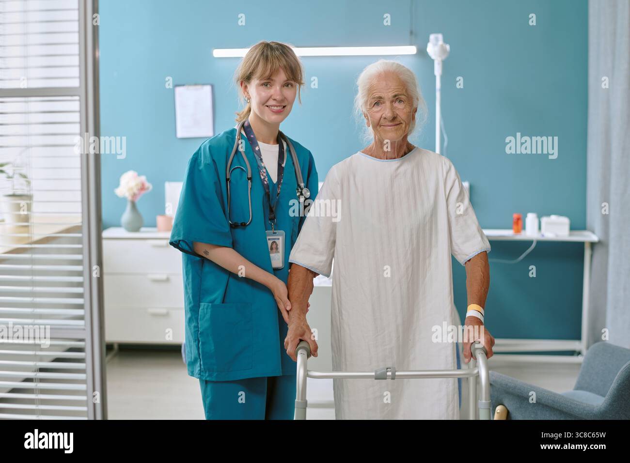 Donna caucasica anziana che usa Walker assistita da giovane infermiera donna adulta sorridente Foto Stock