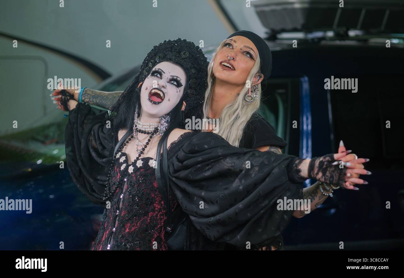 due donne gotiche si mettono in posa in modo giocoso ed espressivo con un trucco elaborato e abiti scuri. uno indossa zanne di vampiro e una corona, l'altro ha una lunga bionda Foto Stock