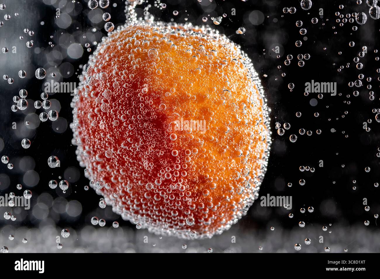 Un'albicocca colorata è immersa nell'acqua e ricoperta di bolle Foto Stock