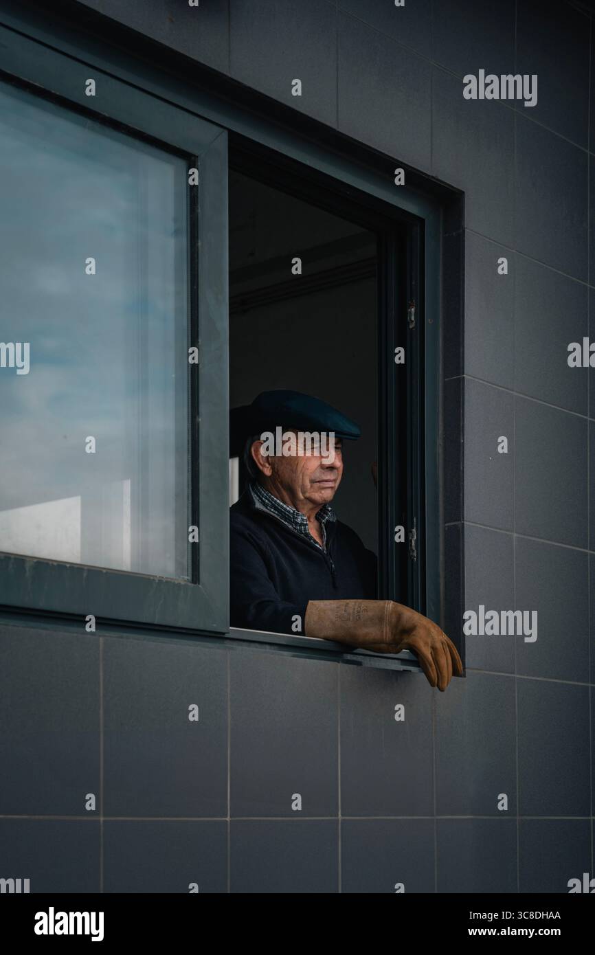 Uomo esperto che guarda fuori dalla finestra dell'edificio di controllo del porto. Portogallo settentrionale, vita costiera, industria marittima, sguardo attento, osservazione Foto Stock