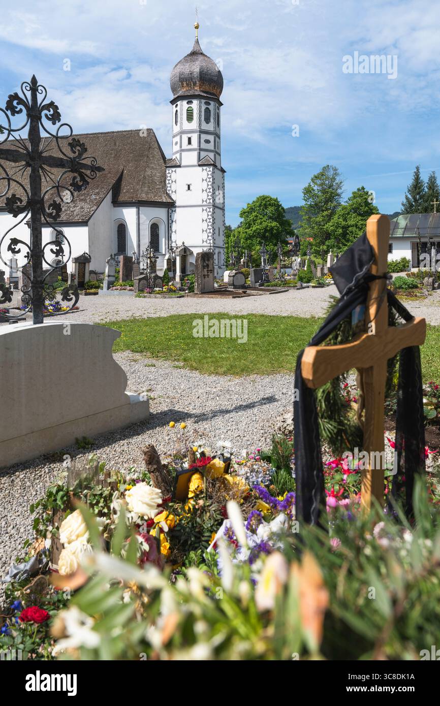 Tomba fresca con decorazioni floreali nel cimitero di fronte alla chiesa bianca di protezione di Santa Maria a Fischbachau, Baviera, Germania Foto Stock