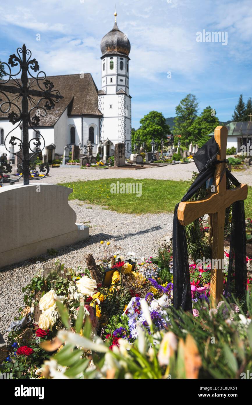Tomba fresca con decorazioni floreali nel cimitero di fronte alla chiesa bianca di protezione di Santa Maria a Fischbachau, Baviera, Germania Foto Stock