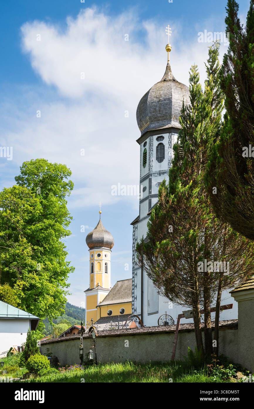 Cimitero con la chiesa bianca della protezione di Maria di fronte alla chiesa gialla del monastero di San Martino a Fischbachau, Baviera, Germania Foto Stock