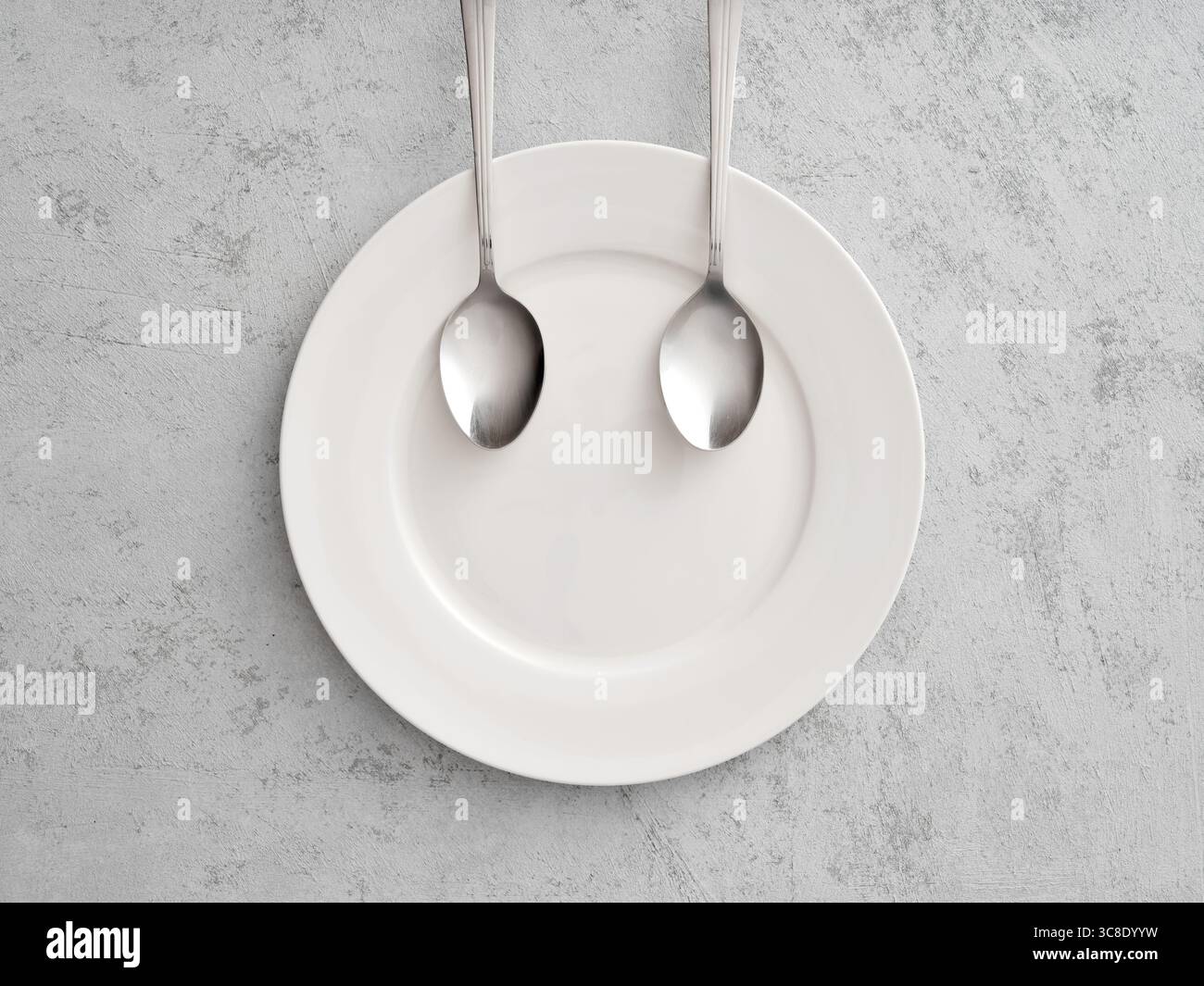 Due cucchiai formano un volto sorridente su un piatto bianco su sfondo grigio, che rappresenta la felicità e la soddisfazione con il cibo Foto Stock Due cucchiai formano un volto sorridente su un piatto bianco su sfondo grigio, che rappresenta la felicità e la soddisfazione con il cibo Foto Stock