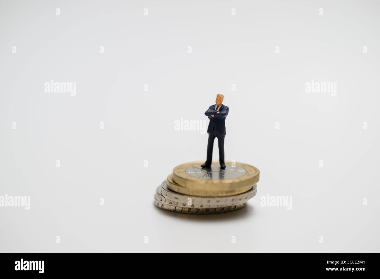, Eine Miniaturfigur eines Geschäftsmanns steht auf einem Stapel Euromünzen. DAS Symbolbild thematisiert wirtschaftliche Macht, Reichtum und Führungsa Foto Stock