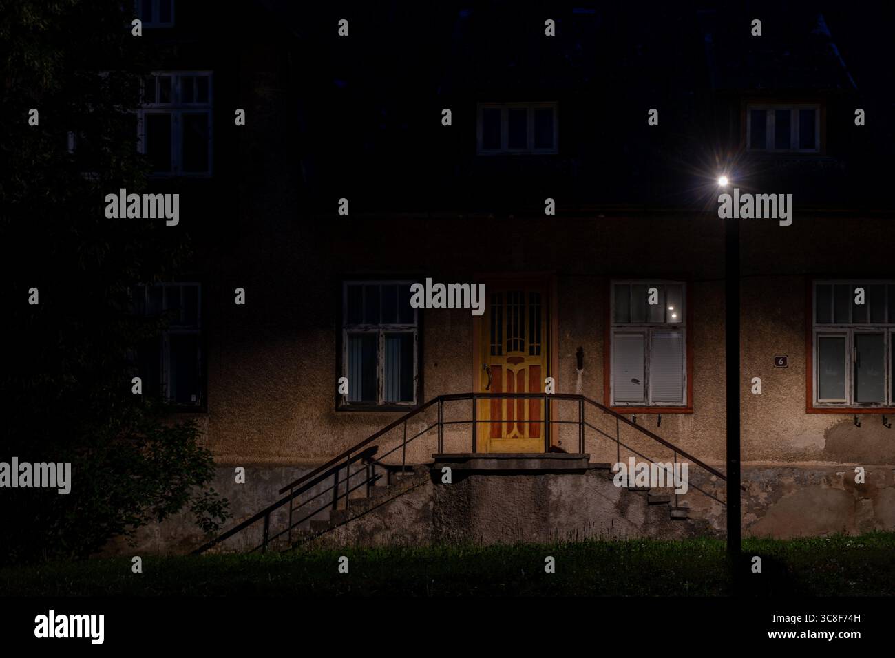 Scena notturna dell'ingresso di un edificio residenziale con porta illuminata e lampione che creano una suggestiva illuminazione a Viljandi, Estonia Foto Stock