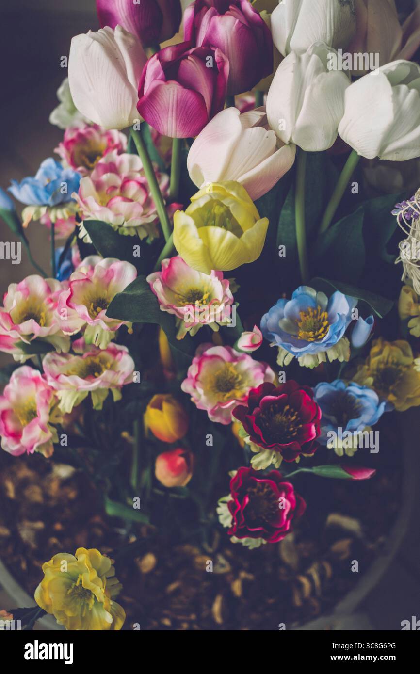 Tulipani artificiali e altri fiori colorati creano una splendida disposizione floreale in un vaso Foto Stock