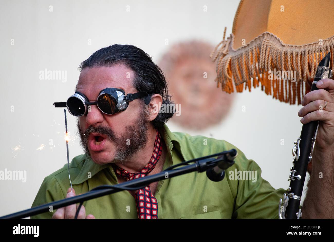 Un musicista jazz offre un'accattivante performance all'aperto, con occhiali di protezione unici e uno sparkler illuminato per un tocco visivo. Foto Stock