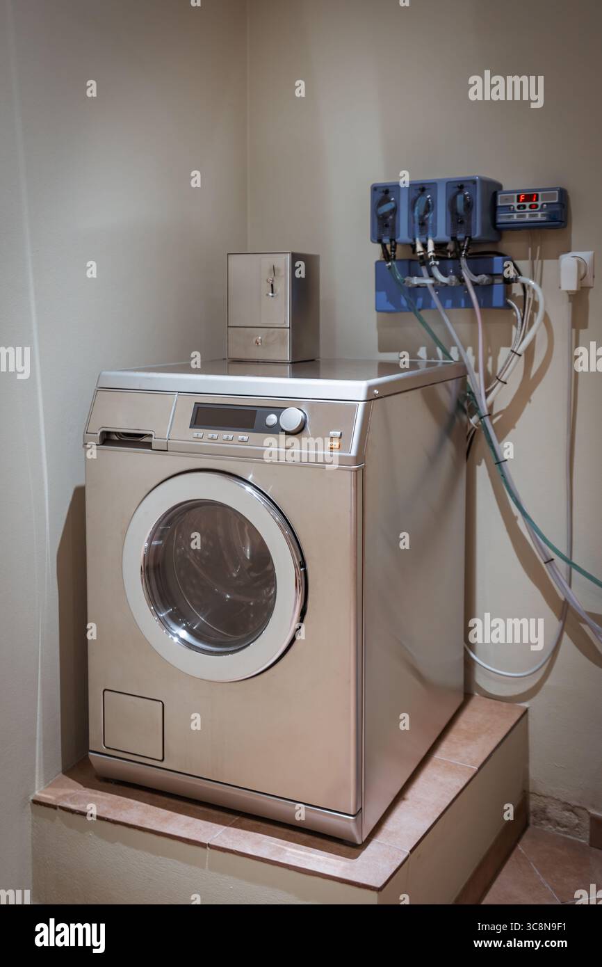 Lavatrice a gettoni in un ostello o nell'area lavanderia albergue, con finiture in acciaio inossidabile, design a carico frontale e detersivo a parete Foto Stock