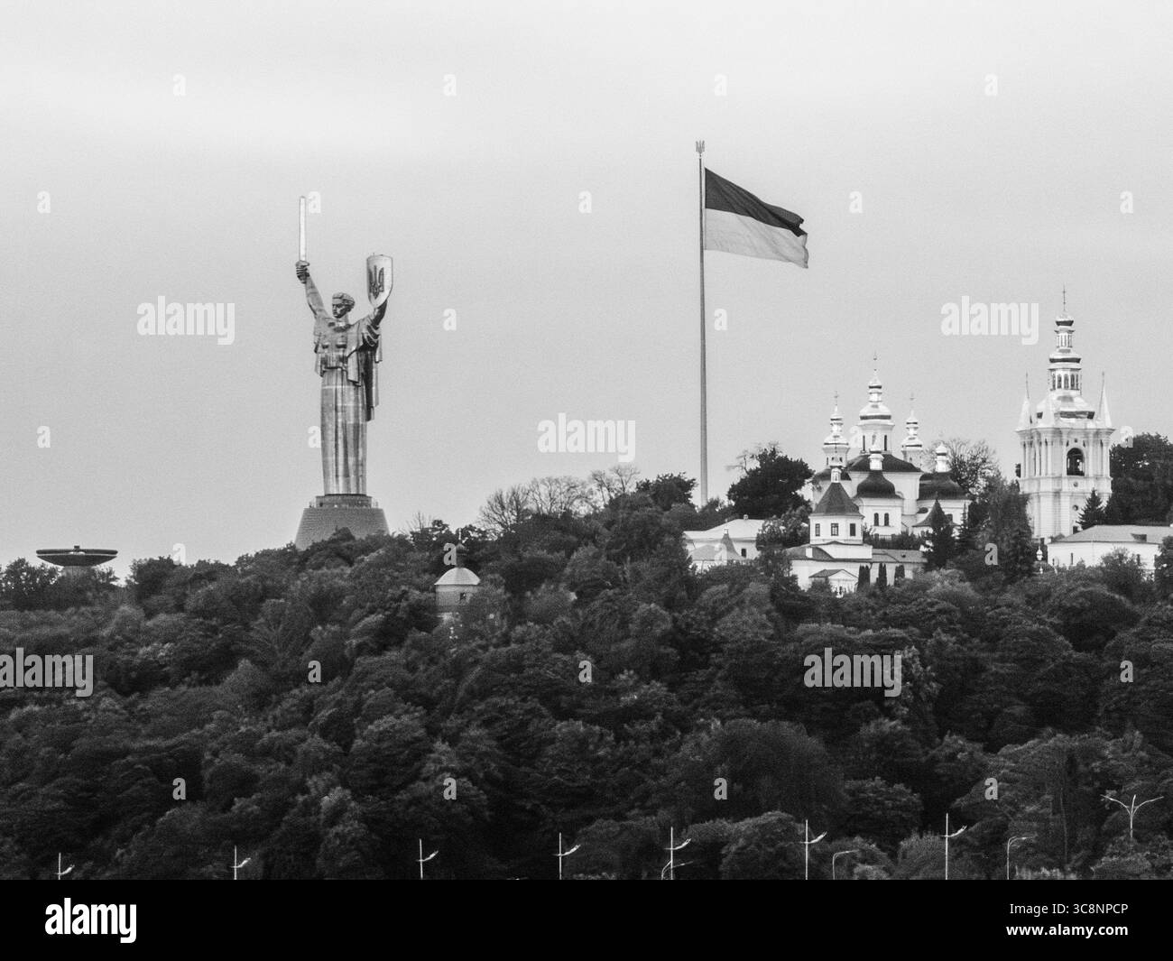 Immagine in bianco e nero che raffigura l'imponente monumento della madre Ucraina che torreggia sopra gli alberi, con spada e scudo, con la bandiera Ucraina e Ky Foto Stock