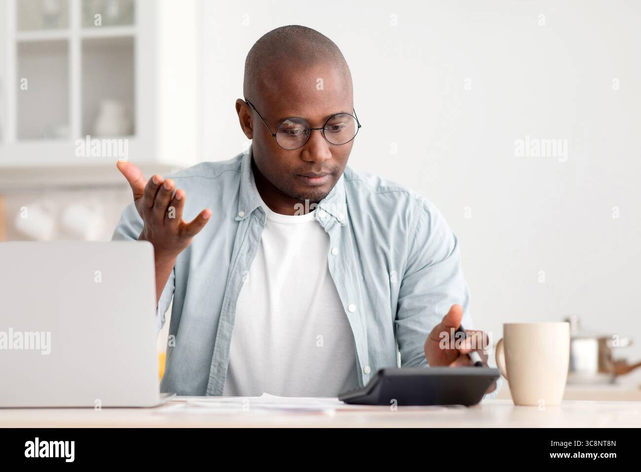 Concetto di risparmio e finanze. Uomo nero scioccato maturo calcolando le fatture, utilizzando la calcolatrice, seduto in cucina Foto Stock