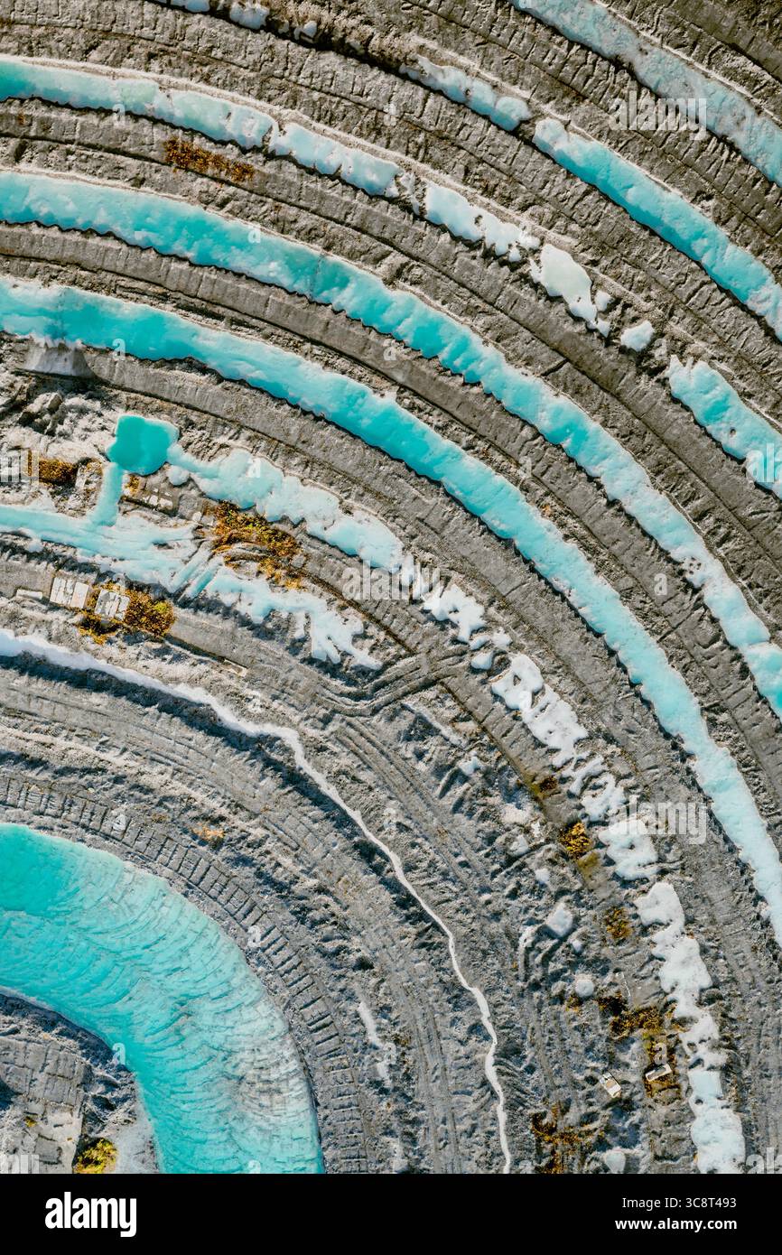 Vista aerea di un vasto paesaggio terrazzato, dove le acque turchesi contrastano con la terra grigia, creando un ipnotico schema di anelli concentrici, Foto Stock