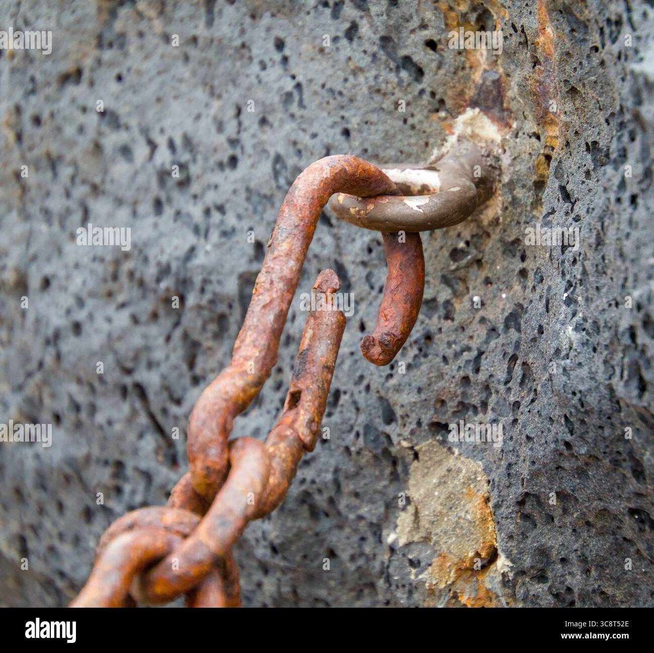 Primo piano di un moschettone pesantemente arrugginito fissato a una catena metallica e ad un anello di ancoraggio montato a parete. Foto Stock
