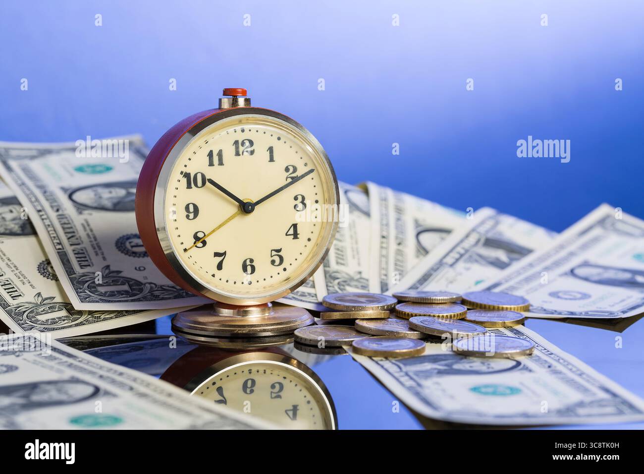 Concetto di business. Il tempo è denaro. Orologio d'epoca vicino al dollaro americano in contanti e monete con un bel sfondo blu sfumato. Foto Stock