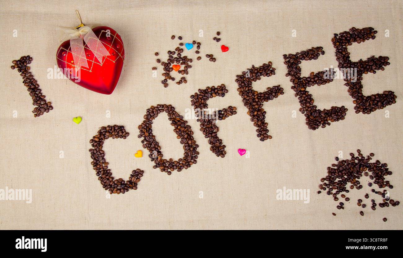 L'iscrizione a base di chicchi di caffè dice che adoro il caffè con simboli a forma di cuore sullo sfondo della iuta. Foto Stock