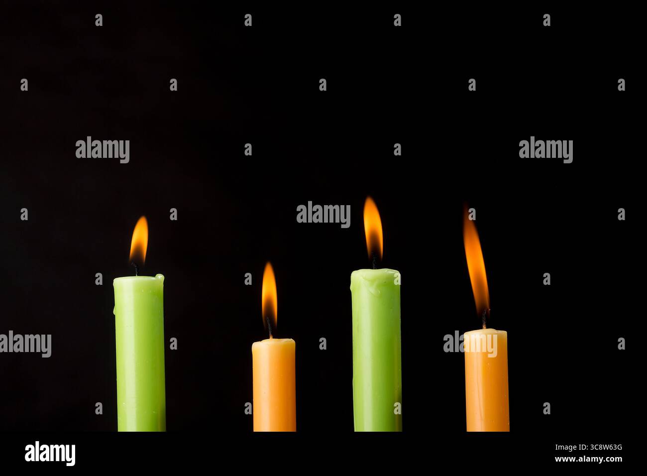 Quattro candele colorate bruciate su sfondo nero. Foto Stock
