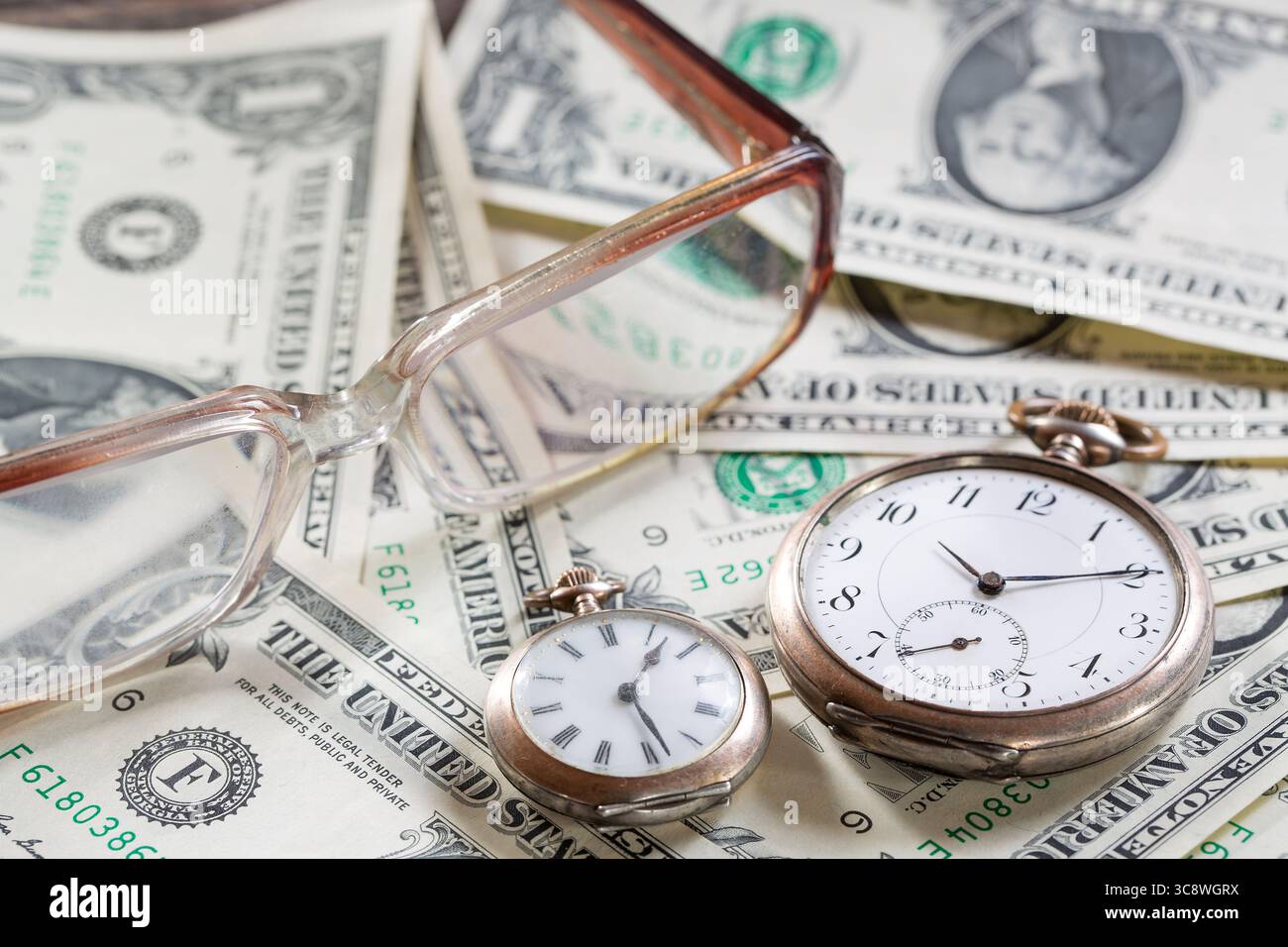 Il tempo è denaro concetto finanziario con vecchi orologi vintage, banconote da un dollaro, occhiali. Foto Stock
