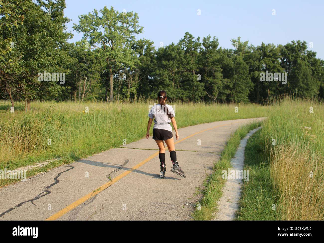 Donna con capelli lunghi su lame a rullo sul North Branch Trail a Miami Woods a Morton Grove, Illinois Foto Stock