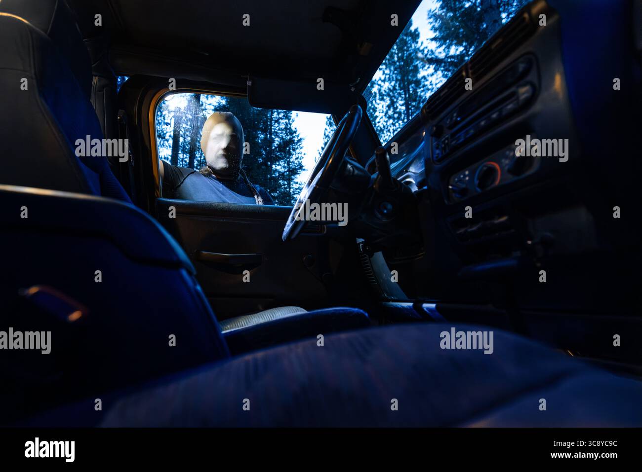Un individuo mascherato emette una torcia elettrica attraverso il finestrino di un'auto mentre sbircia all'interno, suggerendo un tentativo di furto o di furto del veicolo. Foto Stock