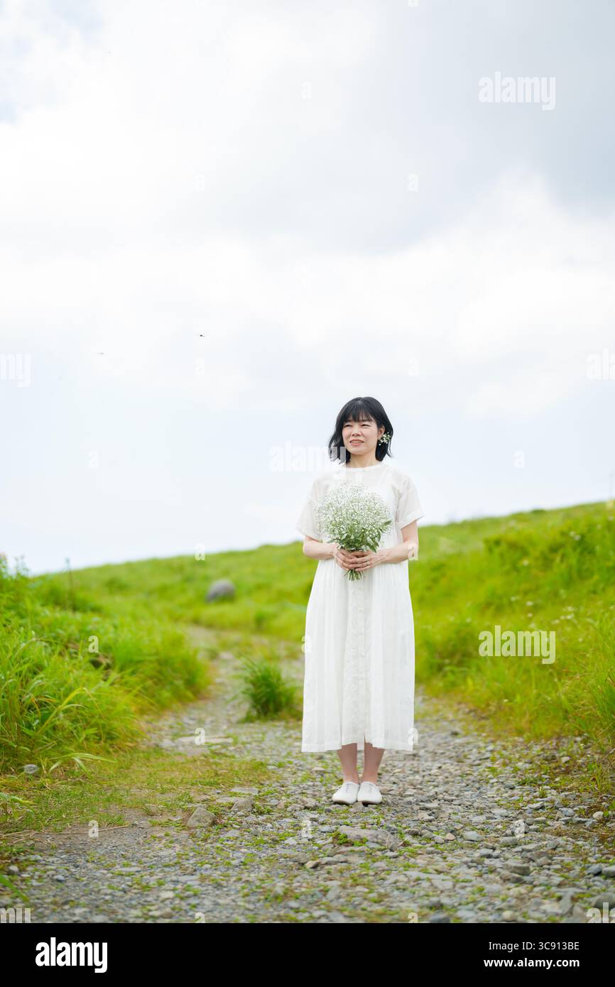 Una donna sui trent'anni con i capelli intermedi in un abito bianco trattiene il respiro del bambino mentre si trova da sola su un sentiero di montagna sotto il cielo aperto, senza edifici. Foto Stock