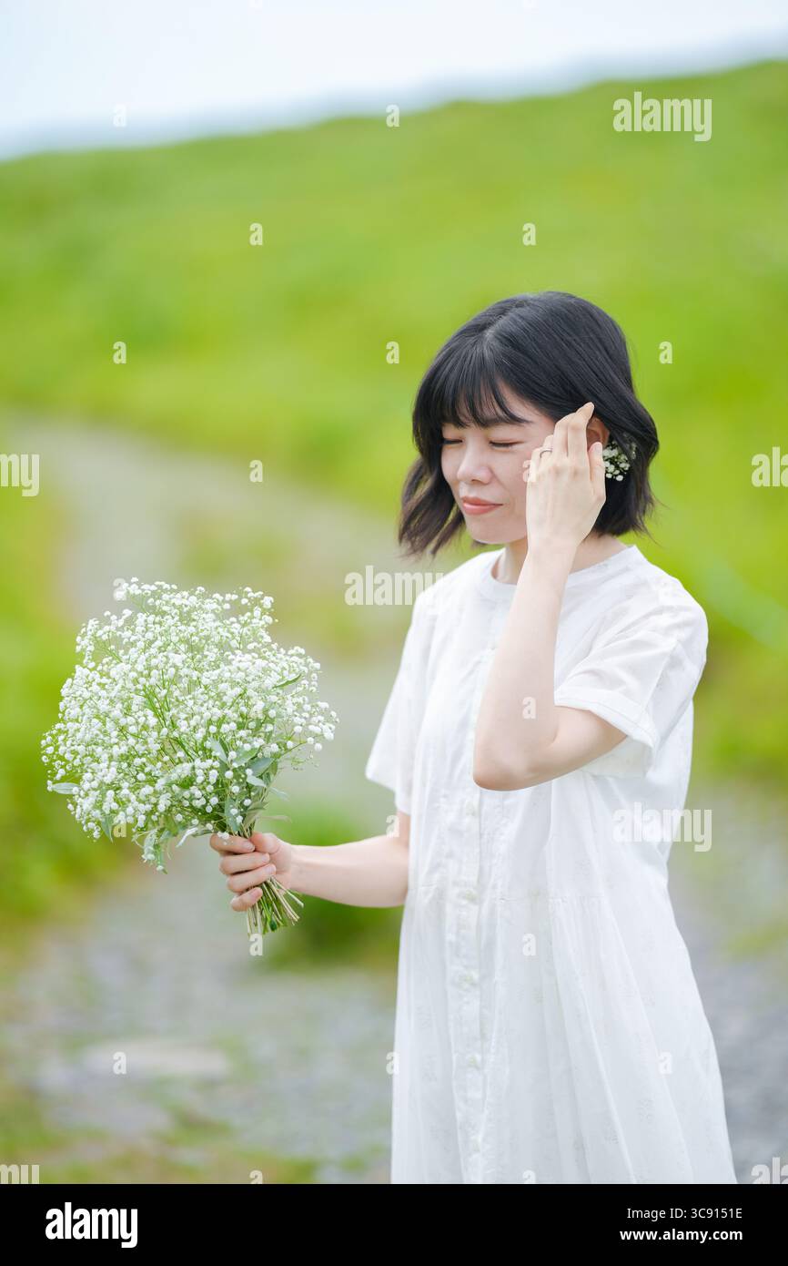 Una donna sui trent'anni con i capelli intermedi in un abito bianco trattiene il respiro del bambino mentre si trova da sola su un sentiero di montagna sotto il cielo aperto, senza edifici. Foto Stock