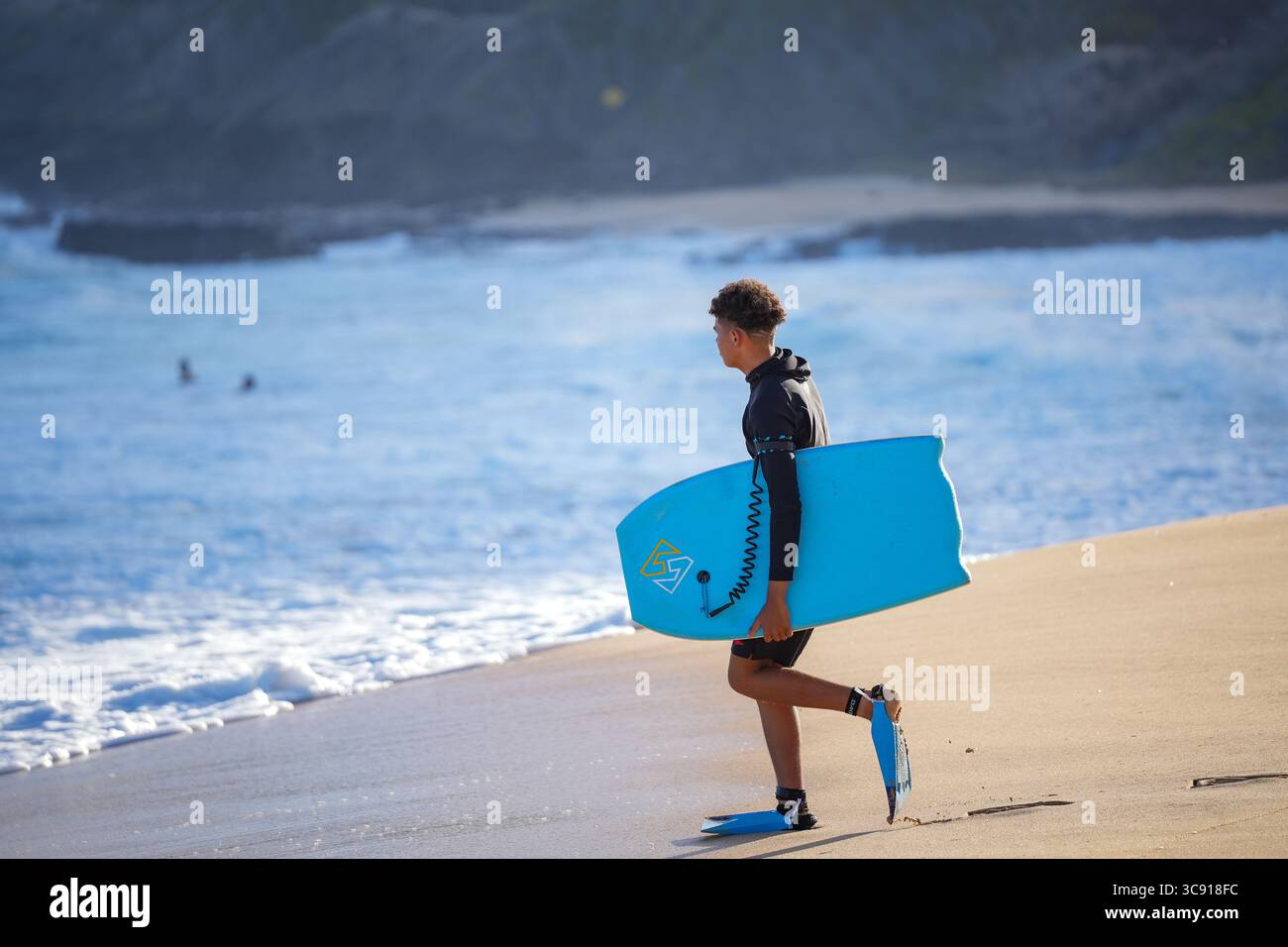 Bodyboarder affronta onde blu torreggianti sotto un cielo luminoso, catturando il brivido e l'energia degli sport oceanici estremi in acque cristalline Foto Stock