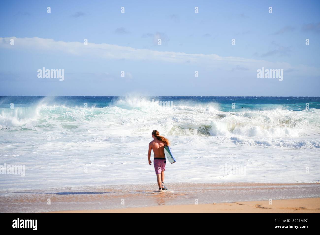 Bodyboarder affronta onde blu torreggianti sotto un cielo luminoso, catturando il brivido e l'energia degli sport oceanici estremi in acque cristalline Foto Stock