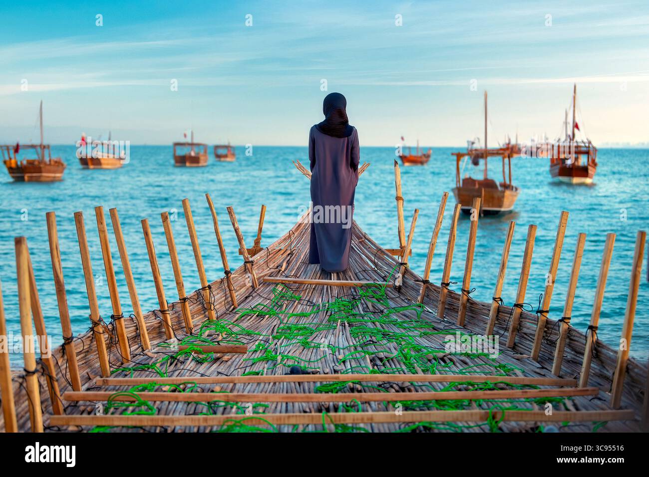 Le donne Abaya si trovano a prua di una tradizionale barca da pesca in legno, affacciata su un mare blu calmo punteggiato da barche simili. Foto Stock