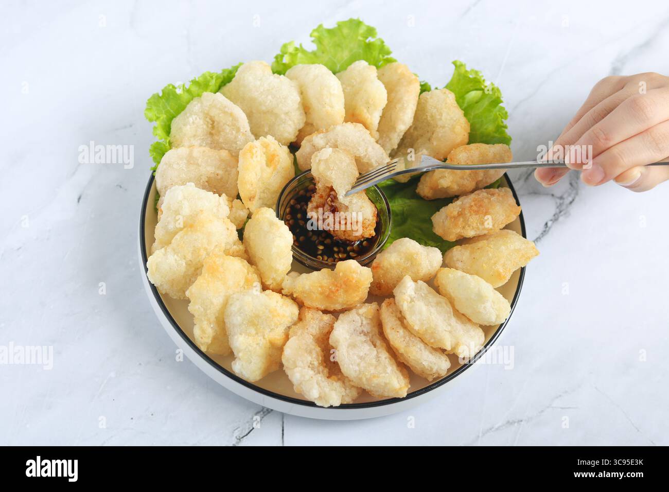 Persona che tiene la forchetta per mangiare il Cireng, un popolare spuntino indonesiano a base di farina di tapioca, organizzato su un piatto bianco. Al centro c'è una salsa subacquea. Foto Stock