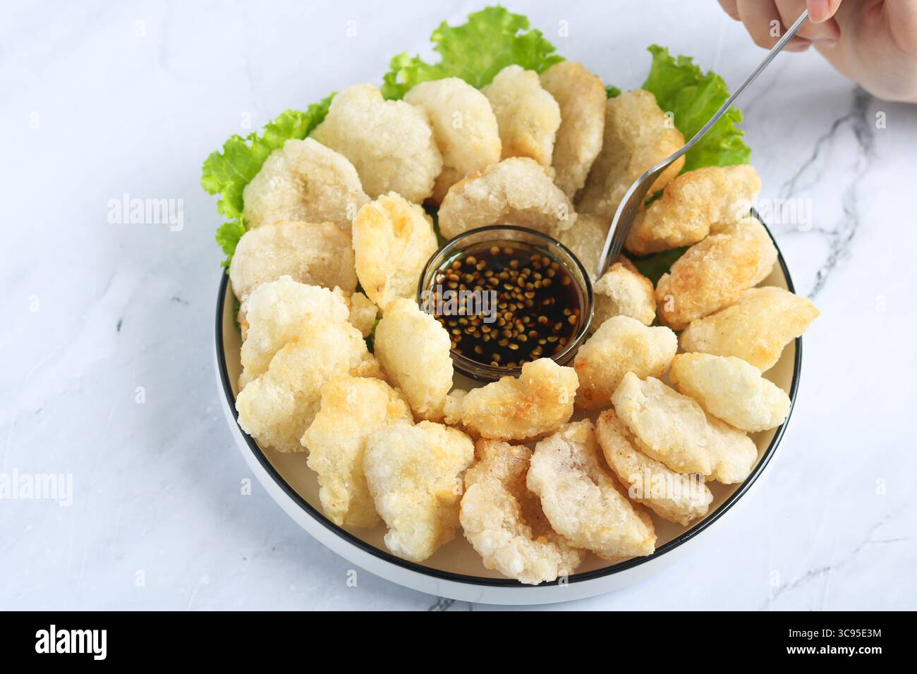Persona che usa la forchetta per mangiare il Cireng, un popolare spuntino indonesiano a base di farina di tapioca, ordinato su un piatto bianco. Accanto c'è una salsa per immersione. Foto Stock