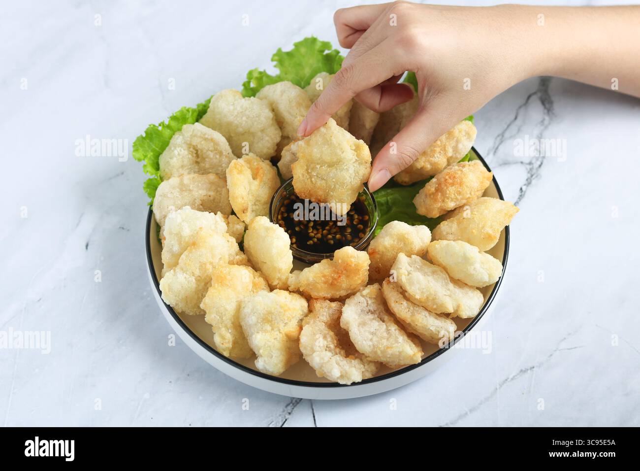 Persona che usa la mano per mangiare il Cireng, un popolare spuntino indonesiano a base di farina di tapioca, ordinato su un piatto bianco. Accanto c'è una salsa per immersione. Foto Stock