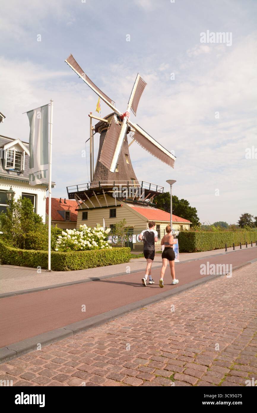 Corridori che passano davanti a uno dei mulini a vento nel Parco Kralingse a Rotterdam, Paesi Bassi Foto Stock
