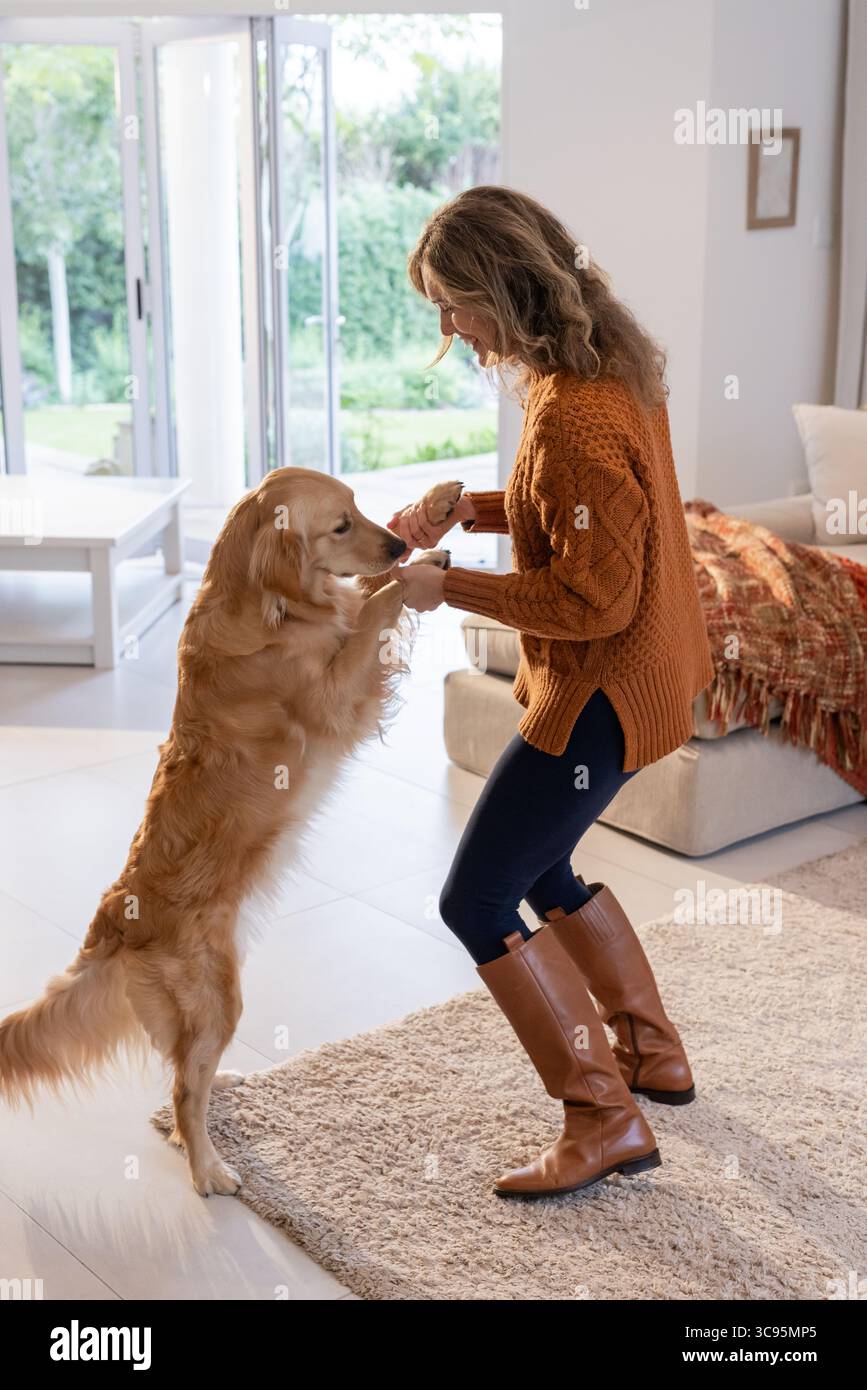 Donna che gioca con Golden retriever su un tappeto beige in un luminoso soggiorno con zampe di cane Foto Stock