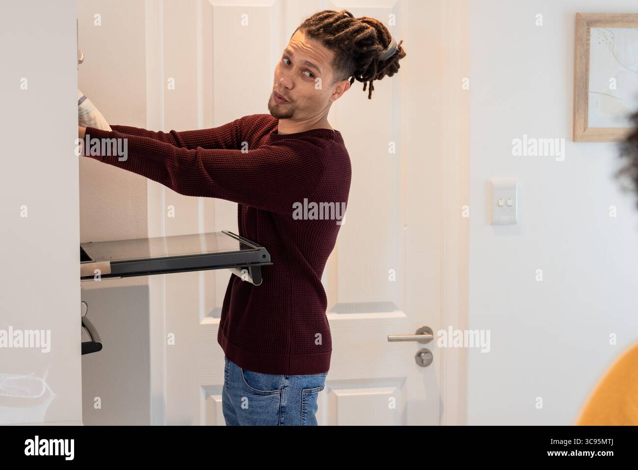 Uomo che indossa guanti da lavoro che estrae il rack estraibile dall'armadietto in cucina, spazio di copia Foto Stock