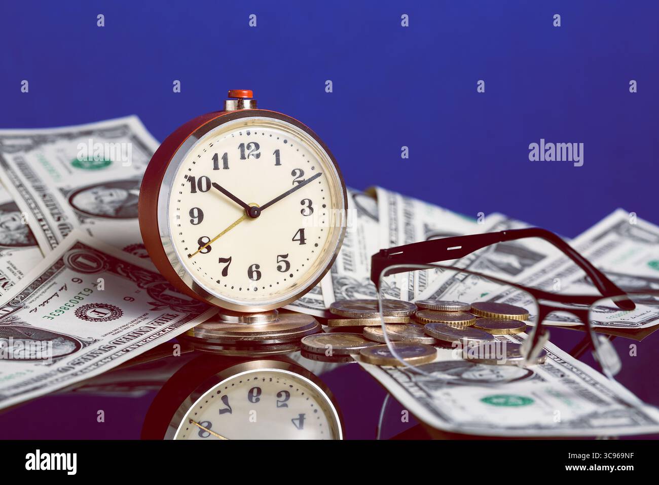 Il tempo è un concetto di denaro con un vecchio orologio d'epoca, banconote da un dollaro, occhiali e una bella riflessione su sfondo blu. Foto Stock