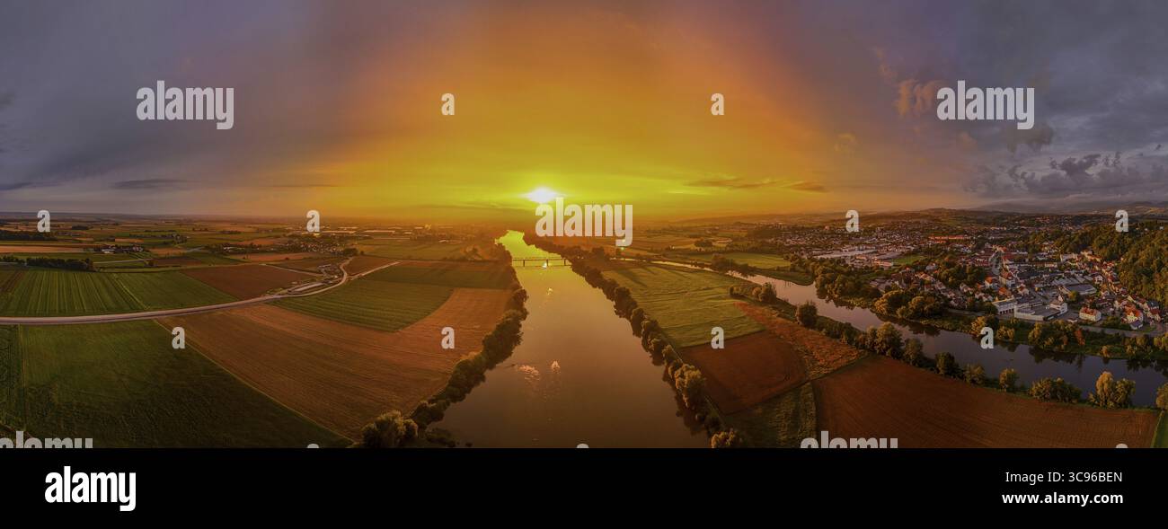 Il sole si abbassa all'orizzonte e bagna il paesaggio con una luce calda. Campi e foreste circondano il tranquillo Danubio nella bassa Baviera, mentre il colo Foto Stock