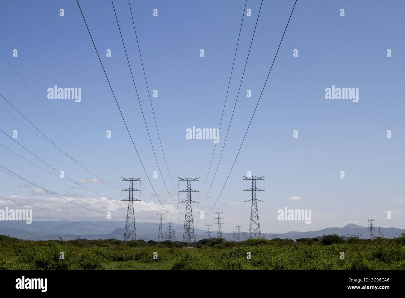 Vista delle linee elettriche che si estendono attraverso un paesaggio verde vivace sotto un cielo azzurro, una testimonianza delle infrastrutture energetiche, Suswa, Narok, Kenya. Foto Stock