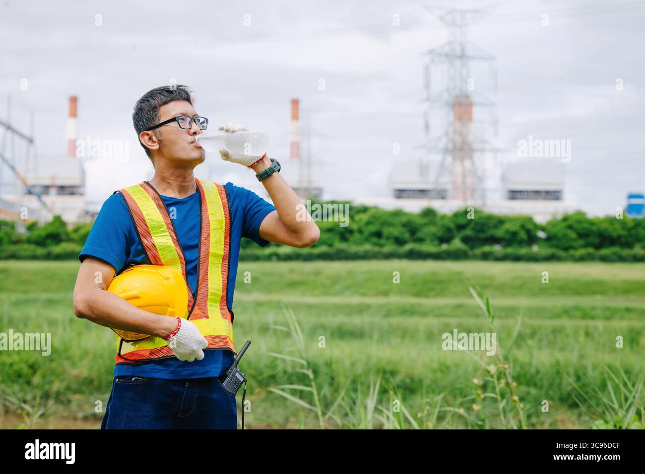 Ingegnere lavoratore asiatico maschio che beve acqua pulita mentre lavora all'aperto, dissetato secco rinfrescante bevanda freno rilassarsi al lavoro Foto Stock