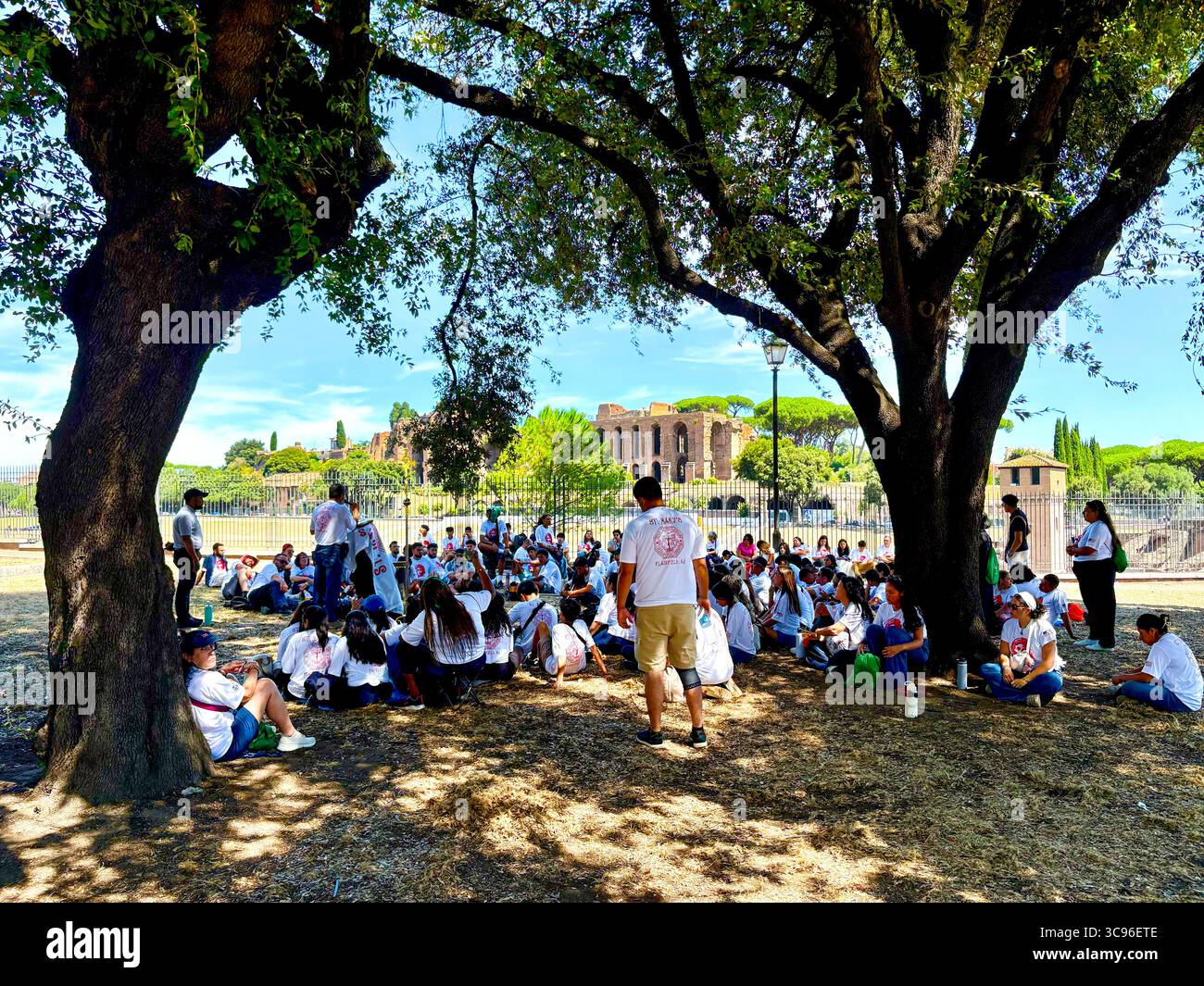 Giovani pellegrini seduti all'ombra vicino al Circo massimo, ascoltando un oratore durante il Giubileo della Gioventù 2025, Roma, Italia. - Immagine stock catturata con smartphone
