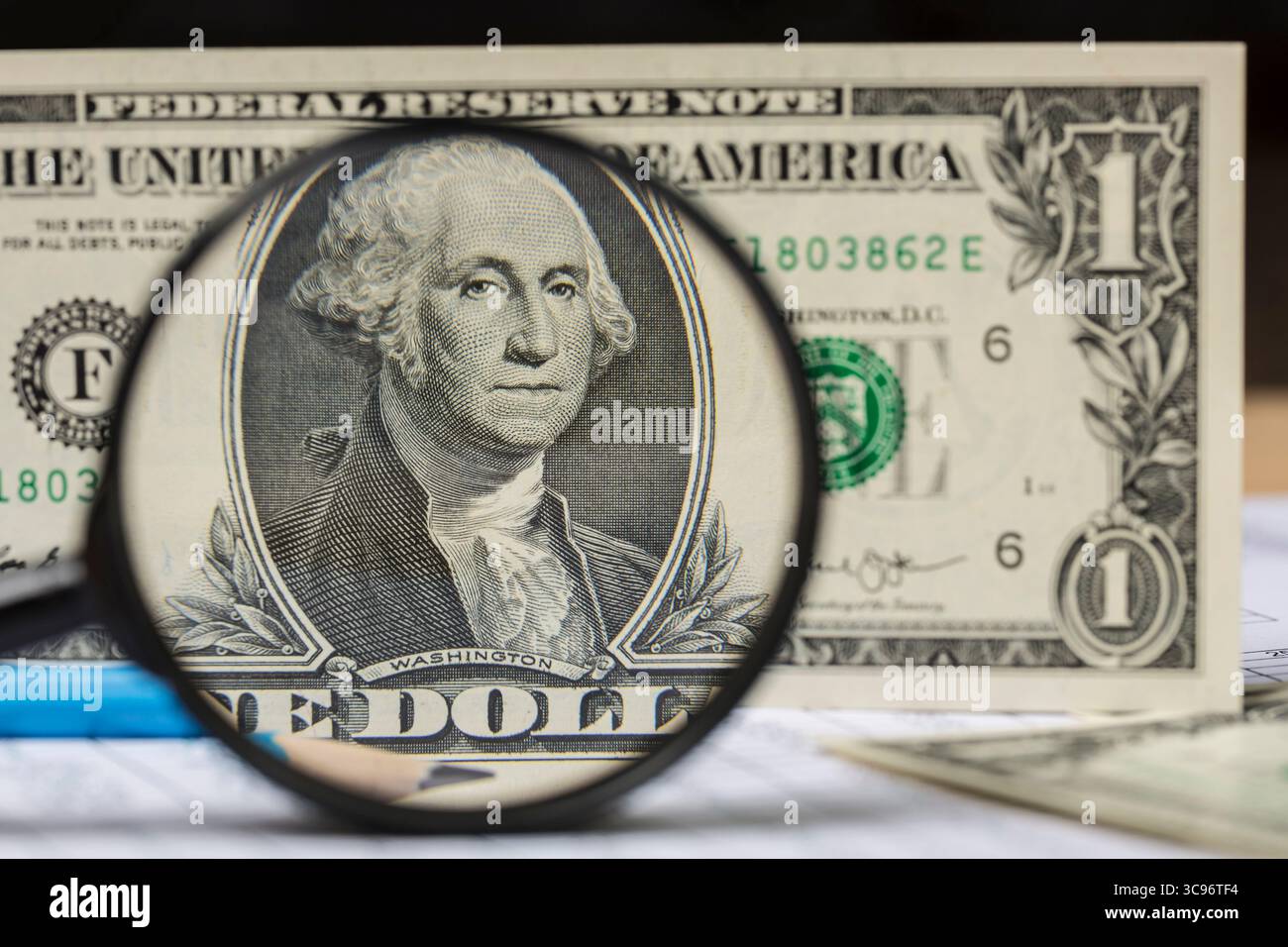 Banconote e matita in dollari americani attraverso una grande lente d'ingrandimento Foto Stock