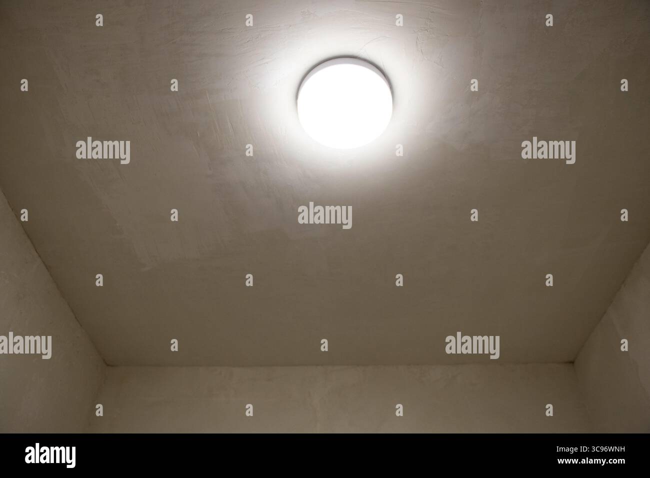 Lampadario luminoso sul soffitto di uno stretto corridoio con pareti beige e stucco, interni di appartamenti con illuminazione e finiture decorative Foto Stock