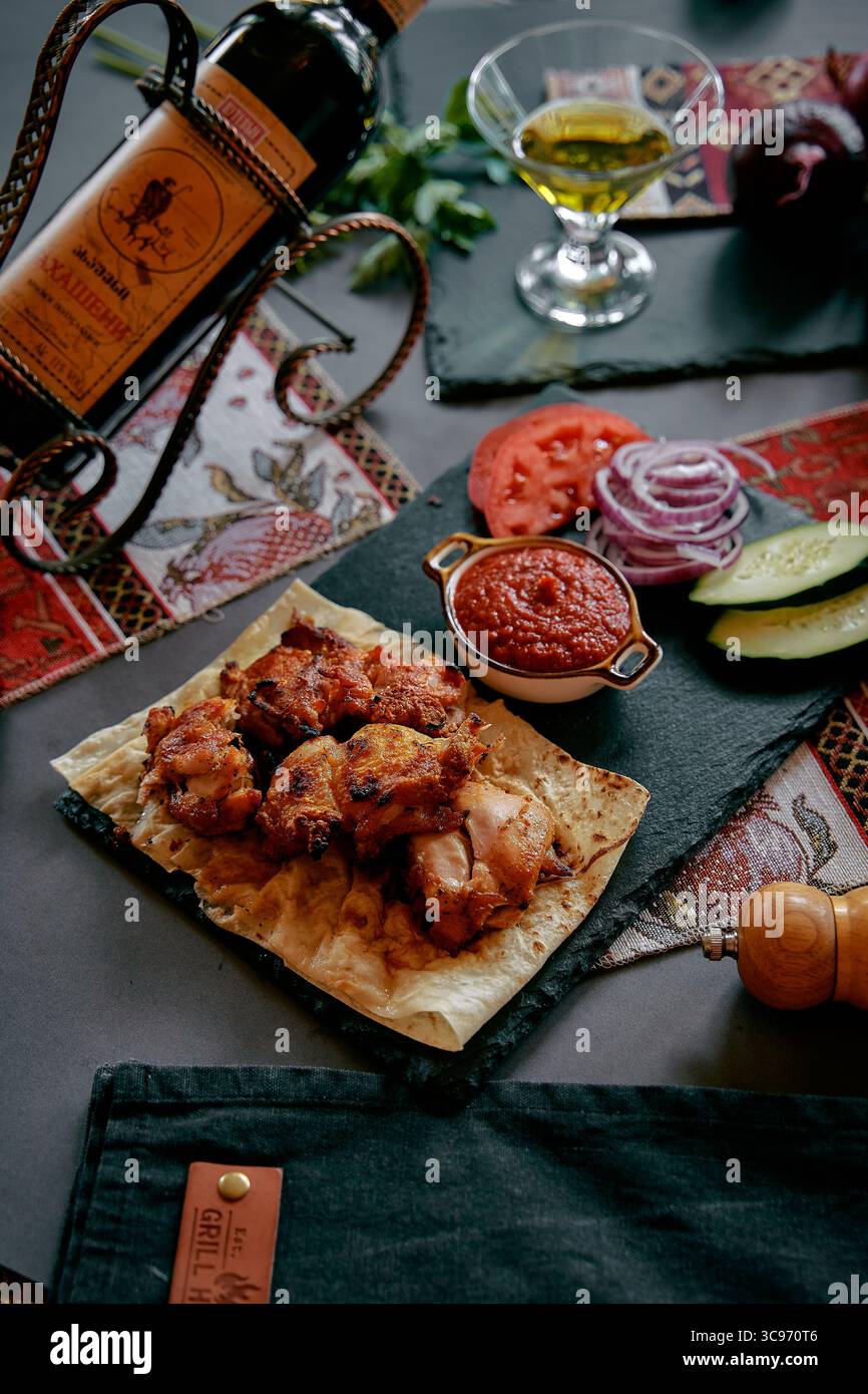 Un delizioso piatto di pollo alla griglia servito su una tavola di ardesia accompagnato da verdure fresche, spezie e salse per un'esperienza culinaria perfetta Foto Stock