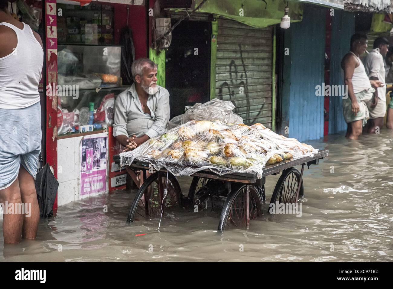 Chattogram, Bangladesh - 5 agosto 2023: Vista di un venditore di strada in mezzo alle inondazioni, il suo carrello carico di merci, una scena toccante di resilienza contro la forza della natura. Foto Stock
