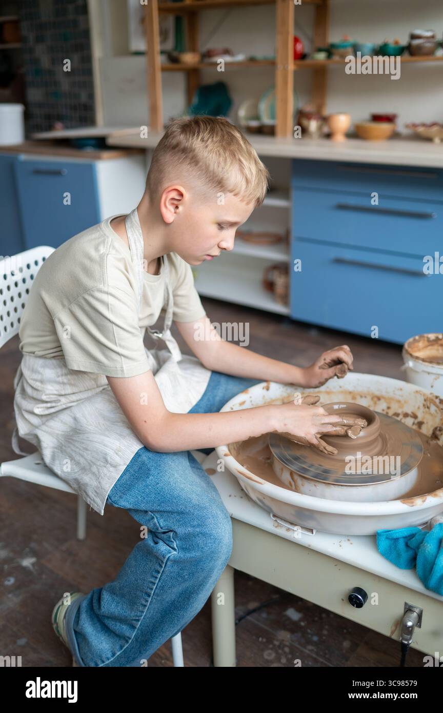 I ragazzi biondi imparano la ceramica, primo piano delle mani che modellano l'argilla su una ruota, attività creative per i bambini in un accogliente studio di ceramica, lavoro di squadra e abilità manuali Foto Stock